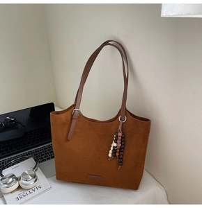 Detail of suede tote bag featuring ethnic bead charm and caramel brown leather straps