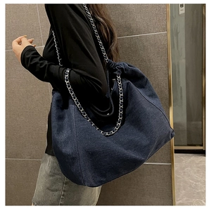 Detail of dark blue denim tote bag featuring silver chain interwoven shoulder strap