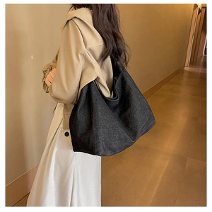 Detailed side view of a large black denim hobo bag worn with a beige trench coat
