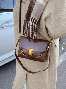 Sac bandoulière marron foncé brillant avec chaîne dorée et boucle sur manteau beige