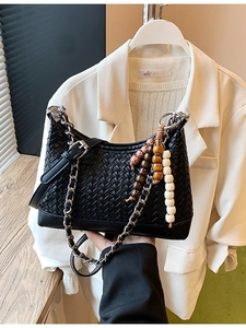 Retro black woven dumpling bag with silver chain and bohemian bead charm on a white blazer