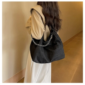 Fashionable black denim tote bag with silver chain strap shown in a minimalist hallway