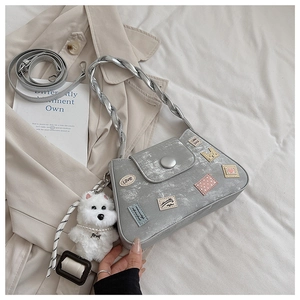 Detalle del bolso de cubo plateado con parches decorativos y colgante de perrito