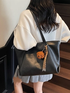 Black matte leather large tote bag with bear charm shown on a shoulder in a stylish indoor setting