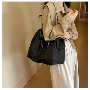 Close-up of black denim tote bag featuring woven metal chain straps and fabric texture