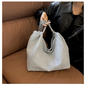 Detail of light blue denim tote bag with silver chain strap on a brown leather sofa