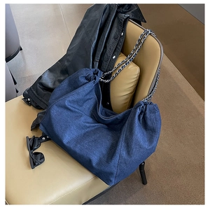 Detailed shot of dark blue denim tote bag with silver chain strap on leather seat