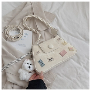 Detalle de bolso saco crema con asa trenzada y amuleto de perro de peluche en gabardina