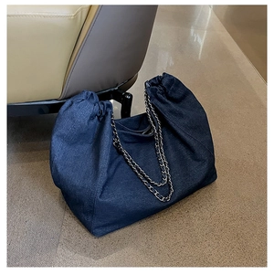 Detailed close-up of blue denim tote bag with leather intertwined metal chain strap