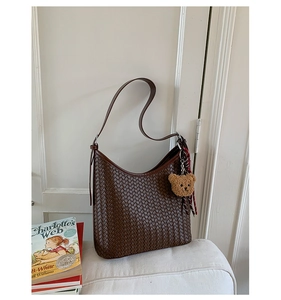 Detail of dark brown woven leather bucket bag with cute plush bear charm on a sofa