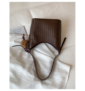 Top view of dark brown woven leather bucket bag with cute bear charm on white fabric