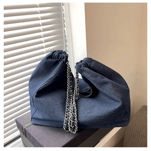 Close-up of dark blue denim cloud bag with dual-tone metal chain on a black gift box