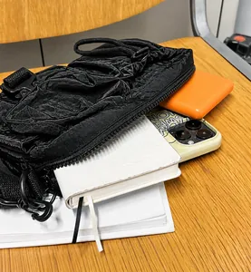 Detail of black nylon crossbody bag showing storage capacity with tech gadgets and zip