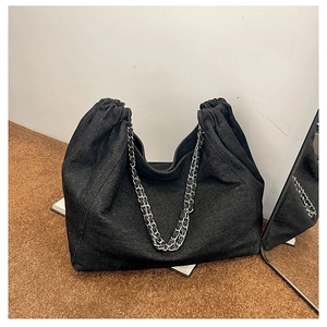 Detail of black denim tote bag featuring silver chain handle and textured fabric