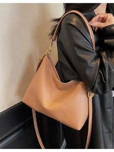 Grand sac cabas tressé caramel avec boucles dorées porté par un mannequin en veste de cuir