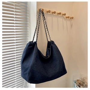 Detail of a large denim tote bag with chain strap hanging on a wooden wall hook