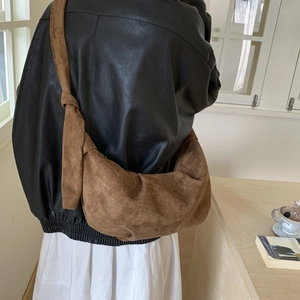 Brown suede crescent bag featuring handcrafted knotted shoulder strap detail on a model
