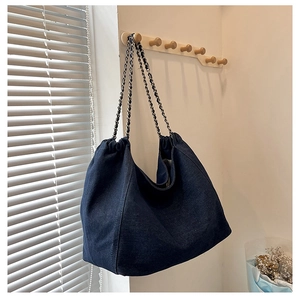 Detail of dark blue denim tote bag with woven chain strap hanging on a wooden wall hook
