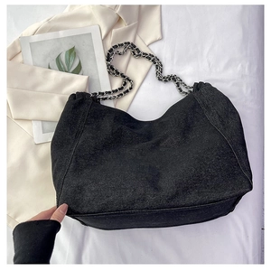 Detail of black denim tote bag with silver chain strap on a minimalist blazer backdrop