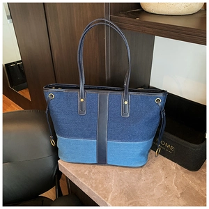 Detail of a large denim tote bag featuring blue patchwork fabric and leather straps