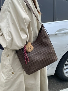Brown woven leather hobo bucket bag with plush bear charm worn by a model in a beige coat