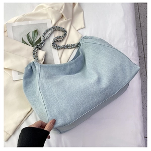 Detail view of light blue denim tote bag with silver chain strap on beige blazer