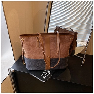 Close-up of color-block denim tote with brown leather handles and gold ring detail