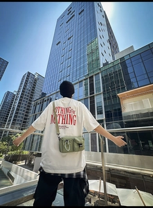 Close-up of white oversized t-shirt and green tactical crossbody bag with multiple pockets
