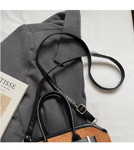 Gros plan du sac bandoulière en daim marron avec garniture en cuir noir et longue sangle