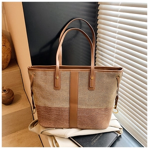 Detail of two-tone canvas and leather tote bag featuring contrast stitching and long handles