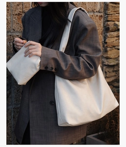 Detail of minimalist cream leather tote bag with matching pouch shown on a gray blazer