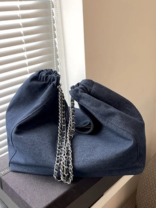 Dark blue denim drawstring hobo bag with classic silver chain strap on a gift box