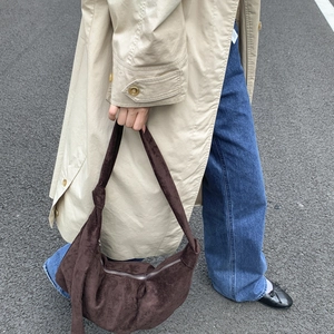 Close-up of dark brown suede hobo bag with knotted strap detail worn with beige trench coat