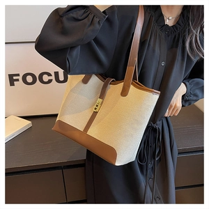 Detail of beige canvas tote bag with brown leather trim and golden metal lock clasp