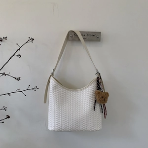 Vue détaillée du sac seau tressé blanc avec texture en cuir et breloque petit ours
