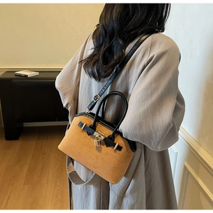 Détail d'un sac shell en daim marron avec cadenas doré et poignée en cuir noir raffiné