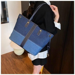 Side view of large denim patchwork tote bag with brown leather straps and metal rivets