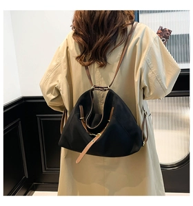 Detail of a large black nylon hobo bag with brown leather strap worn by a model