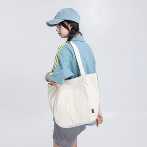 Vue détaillée d'un grand sac cabas en toile blanc cassé porté à l'épaule par un mannequin
