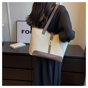 Detail of canvas tote bag with brown leather trim and gold twist lock on model