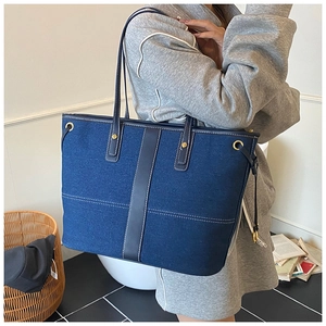 Detail of blue denim tote bag featuring leather straps and white decorative stitching