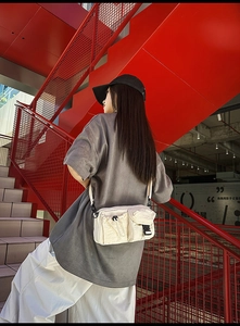 Detail of cream nylon crossbody bag featuring multi-pocket design and quick-release buckles