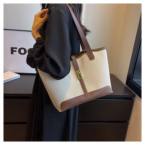 Detail of canvas tote bag showing contrast leather trim and golden twist lock buckle