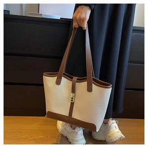 Close-up of canvas tote bag with brown leather trim and golden metal lock detail