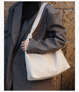 Close-up of white minimalist tote bag with knot shoulder strap on dark blazer