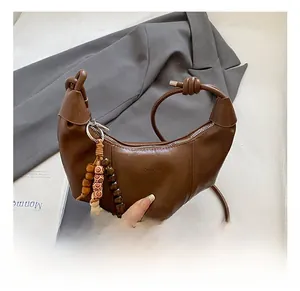 Détail d'un sac demi-lune en cuir marron avec perles décoratives et anse à nœud