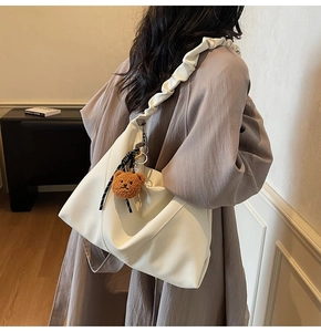 Détail d'un sac cabas blanc en cuir litchi avec bandoulière plissée et breloque ours