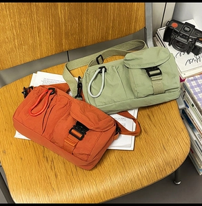 Detail of casual nylon crossbody bags in orange and green on a wooden chair