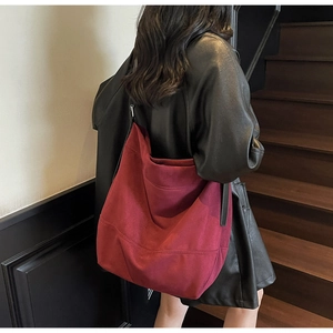 Detail view of large burgundy suede hobo bag worn over the shoulder on leather jacket