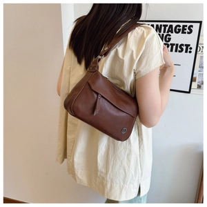 Side view of a brown leather shoulder bag with a silver metal buckle worn by a model